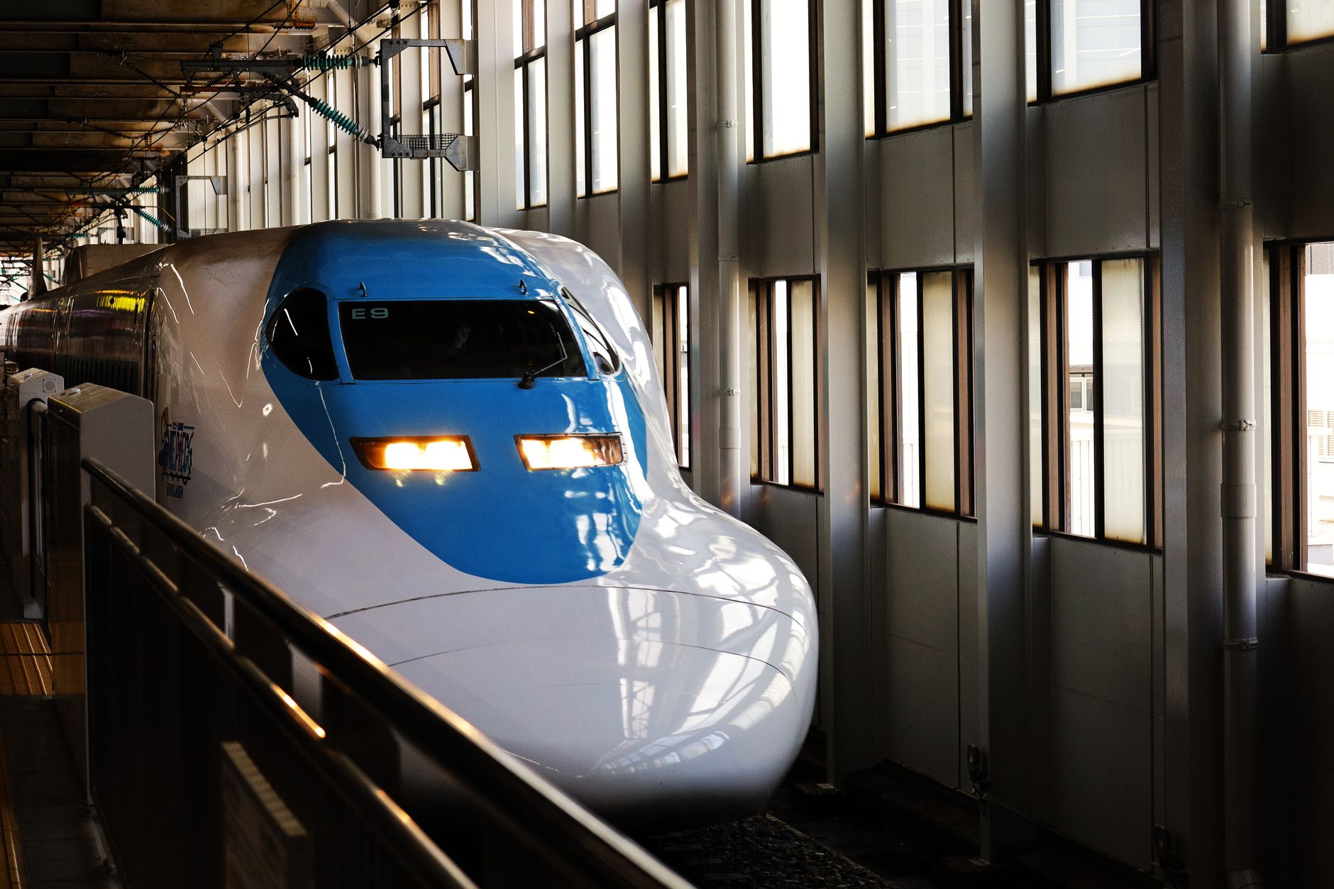 A white and blue shinkansen bullet train arriving at a station platform in Hiroshima, Japan